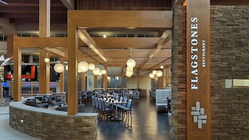 A spacious restaurant interior with high wooden beams, stone accents, and modern pendant lighting.