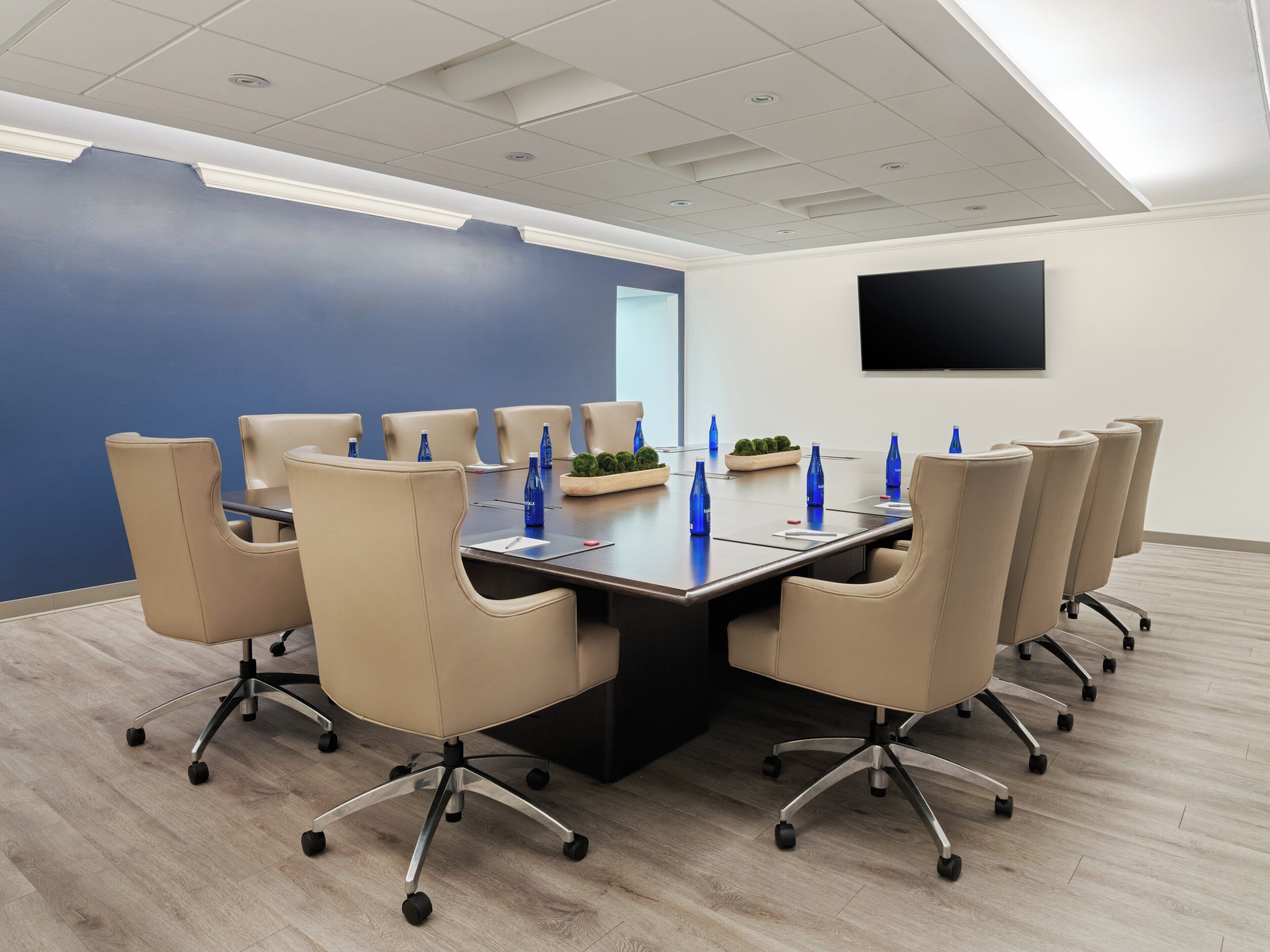 A conference room with a long table, beige chairs, and blue water bottles.