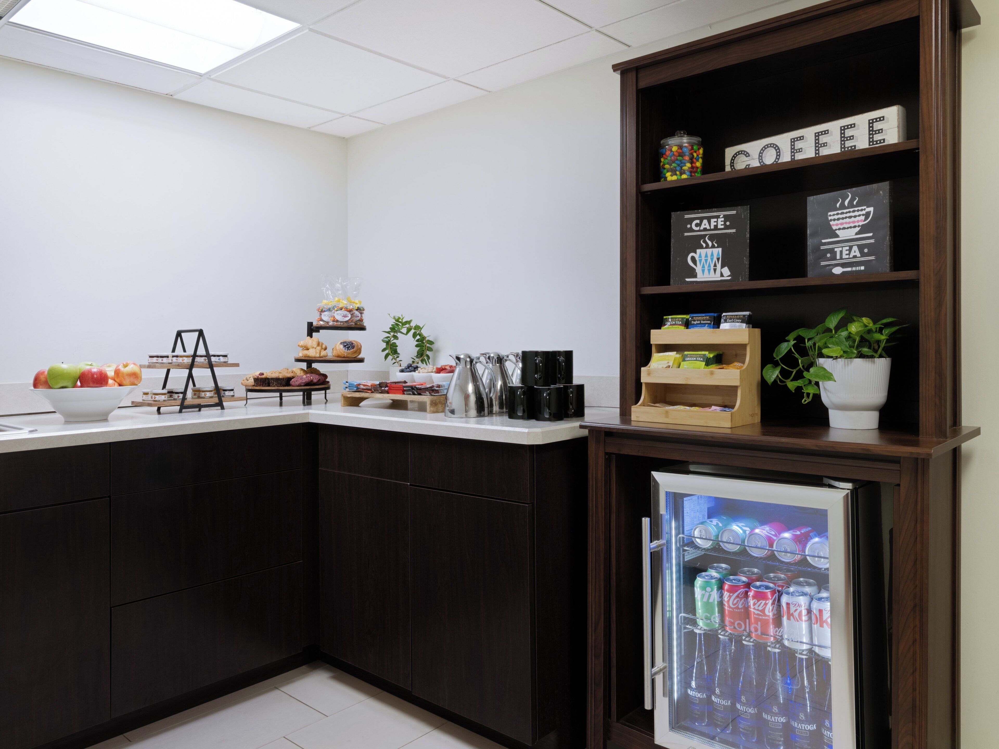 A kitchen with a coffee station, a refrigerator with beverages, and a fruit bowl.