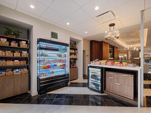 A modern hotel lobby with a self-service beverage station, a small refrigerator, and a reception desk. - Crowne Plaza Suffern - Mahwah by IHG (Suffern)