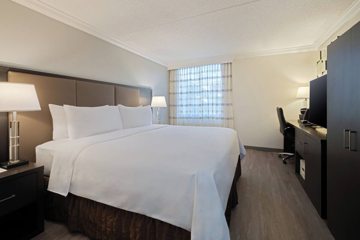 Ein Hotelzimmer mit einem großen Bett, Nachttischen mit Lampen, einem Schreibtisch mit Stuhl und einem Fernseher.