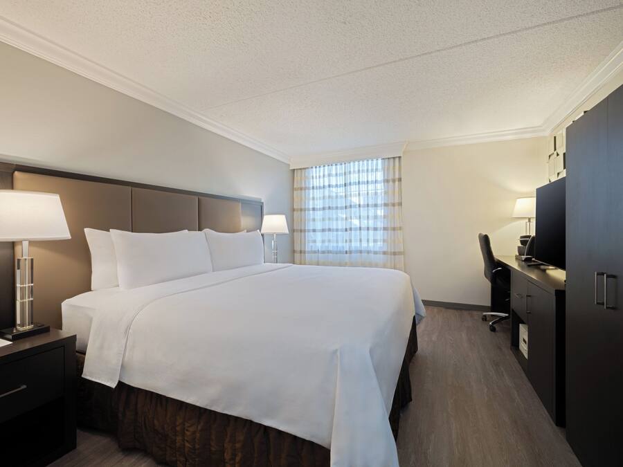 A hotel room with a large bed, bedside tables with lamps, a desk with a chair, and a television.