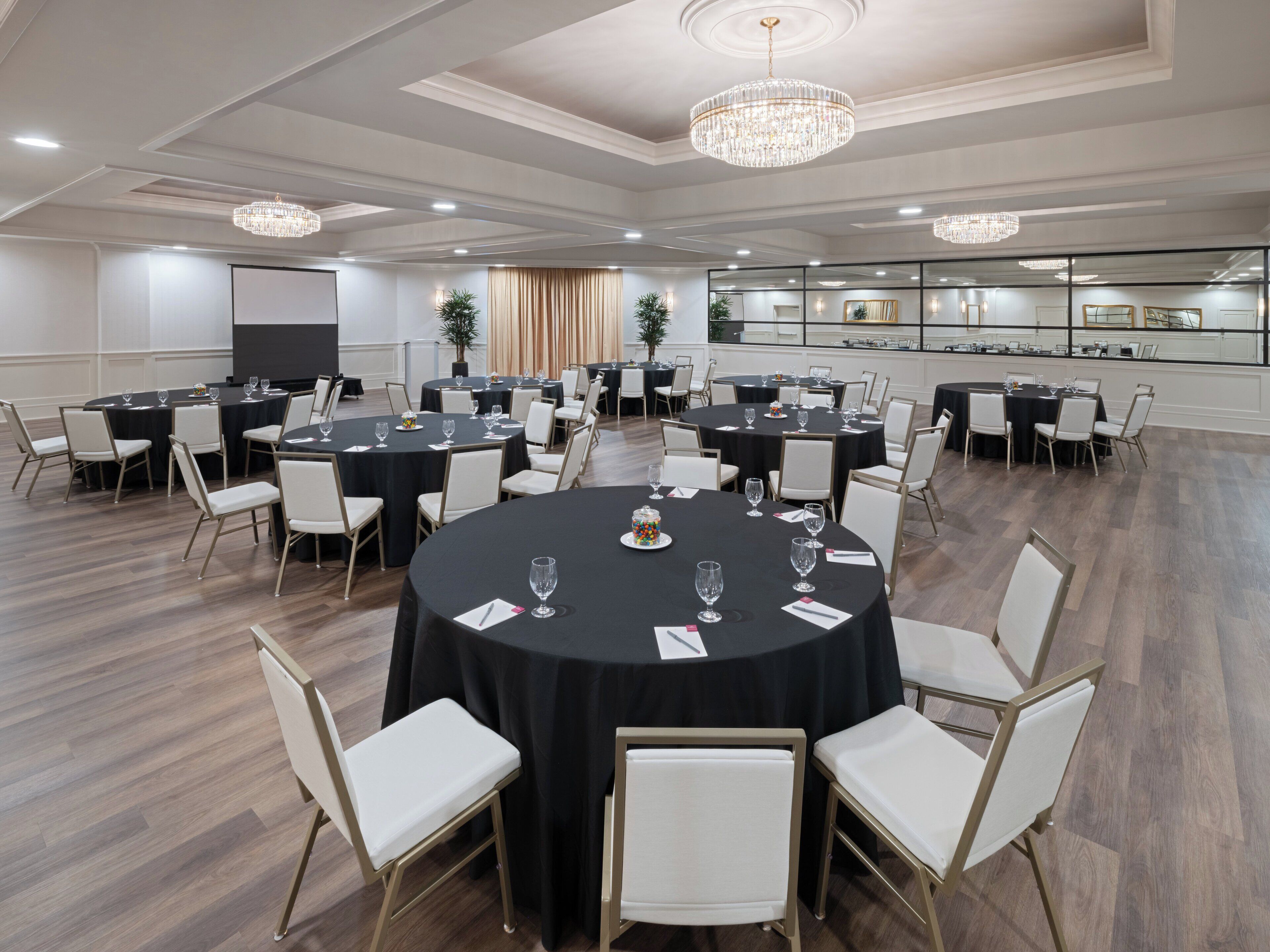 Een vergaderzaal met ronde tafels, witte stoelen en kroonluchters.