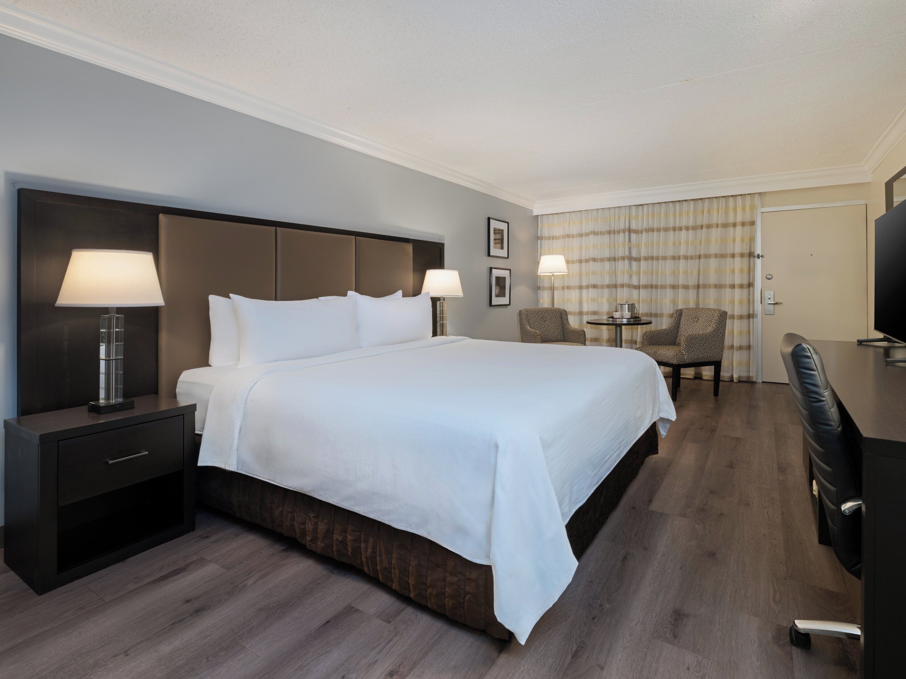 Habitación de hotel con una cama grande, una mesita de noche con lámpara, un escritorio con silla y televisión.