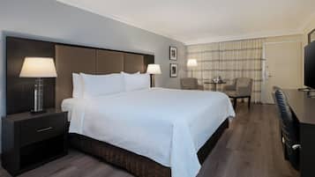 Habitación de hotel con una cama grande, una mesita de noche con lámpara, un escritorio con silla y televisión.