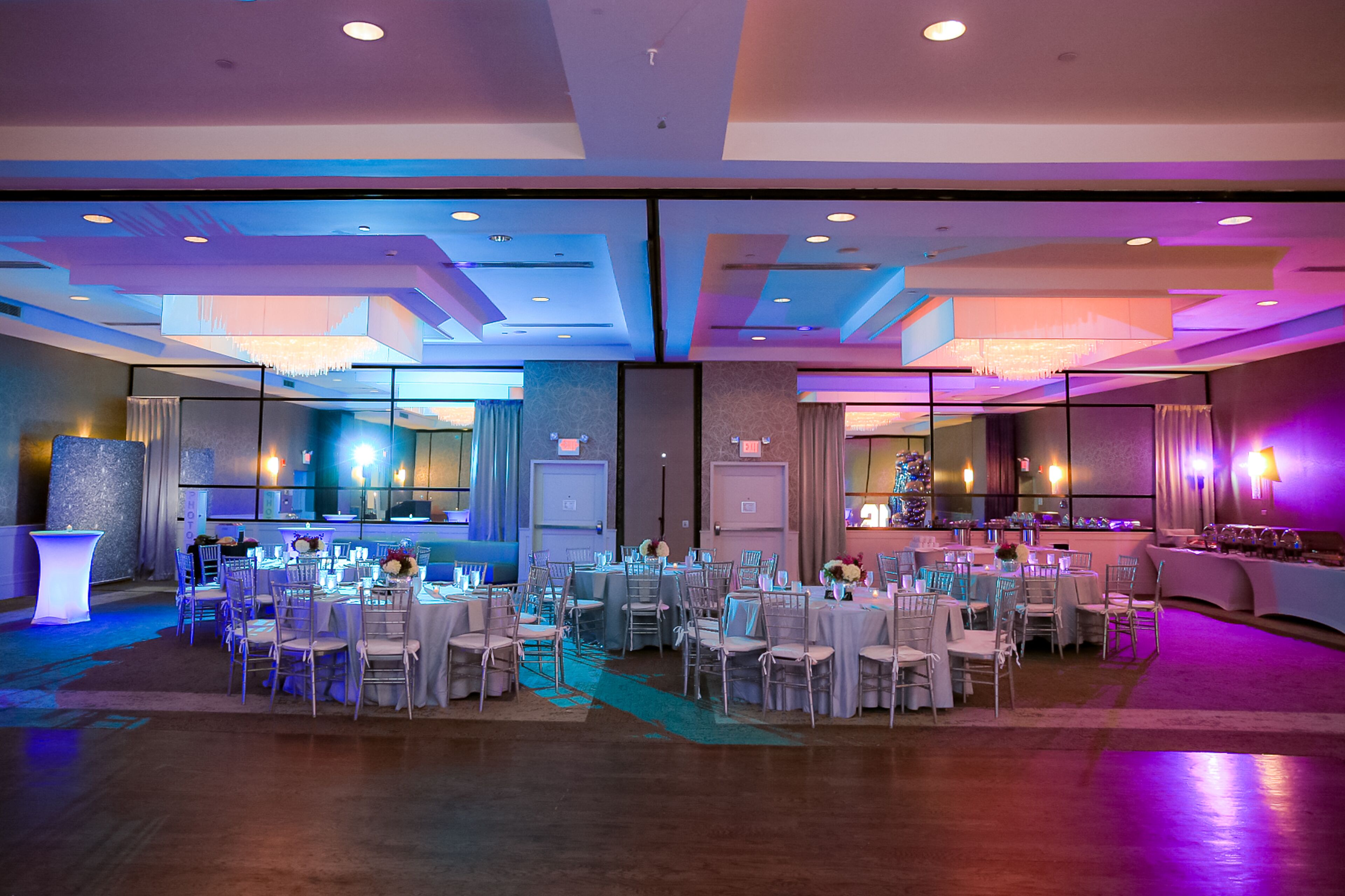 A banquet hall with round tables, chairs, and a bar area.