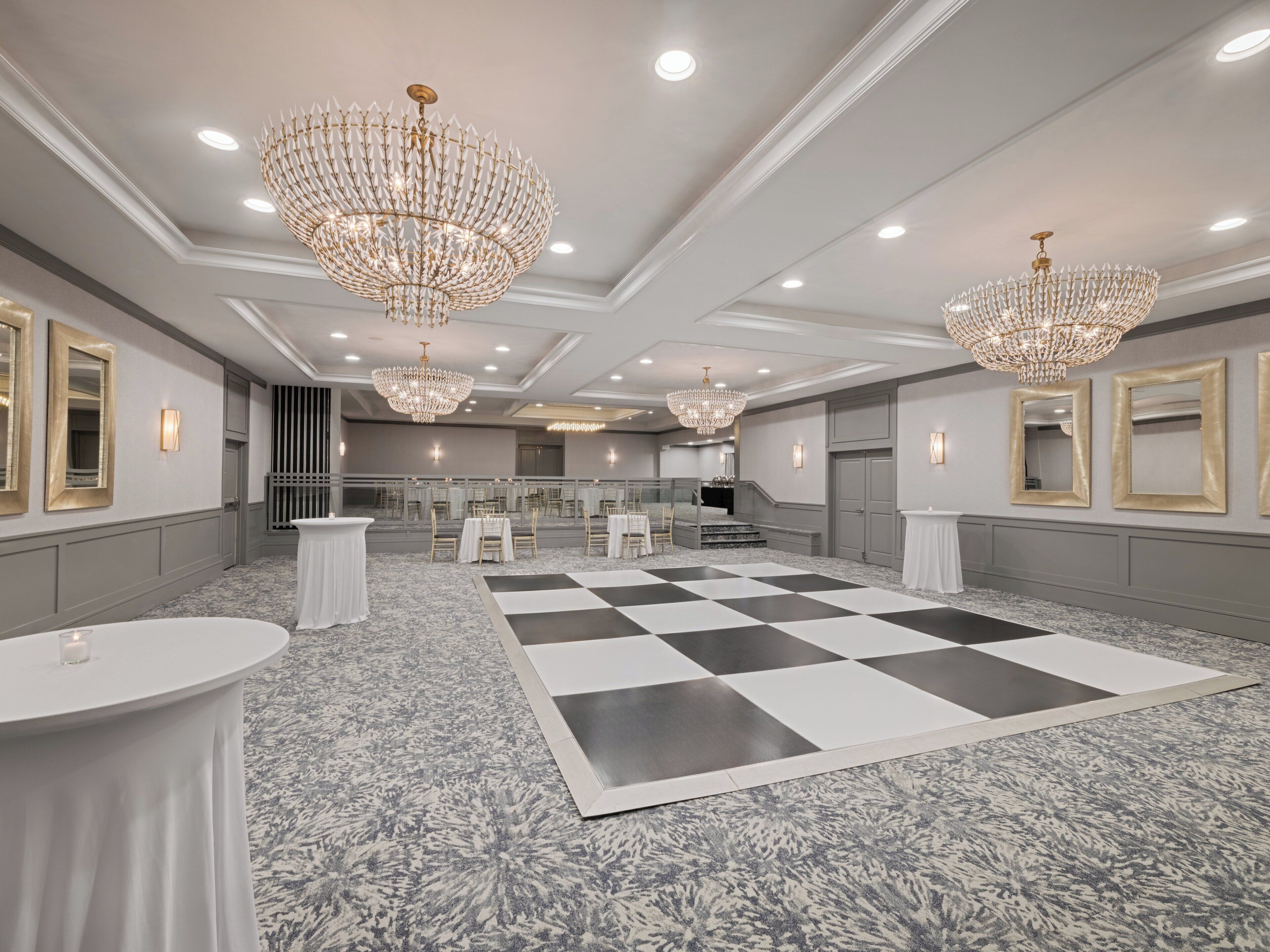 A spacious hotel lobby with a checkered floor, multiple chandeliers, and a grand staircase.