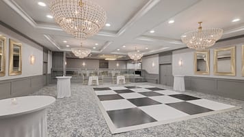 A spacious hotel lobby with a checkered floor, multiple chandeliers, and a grand staircase.