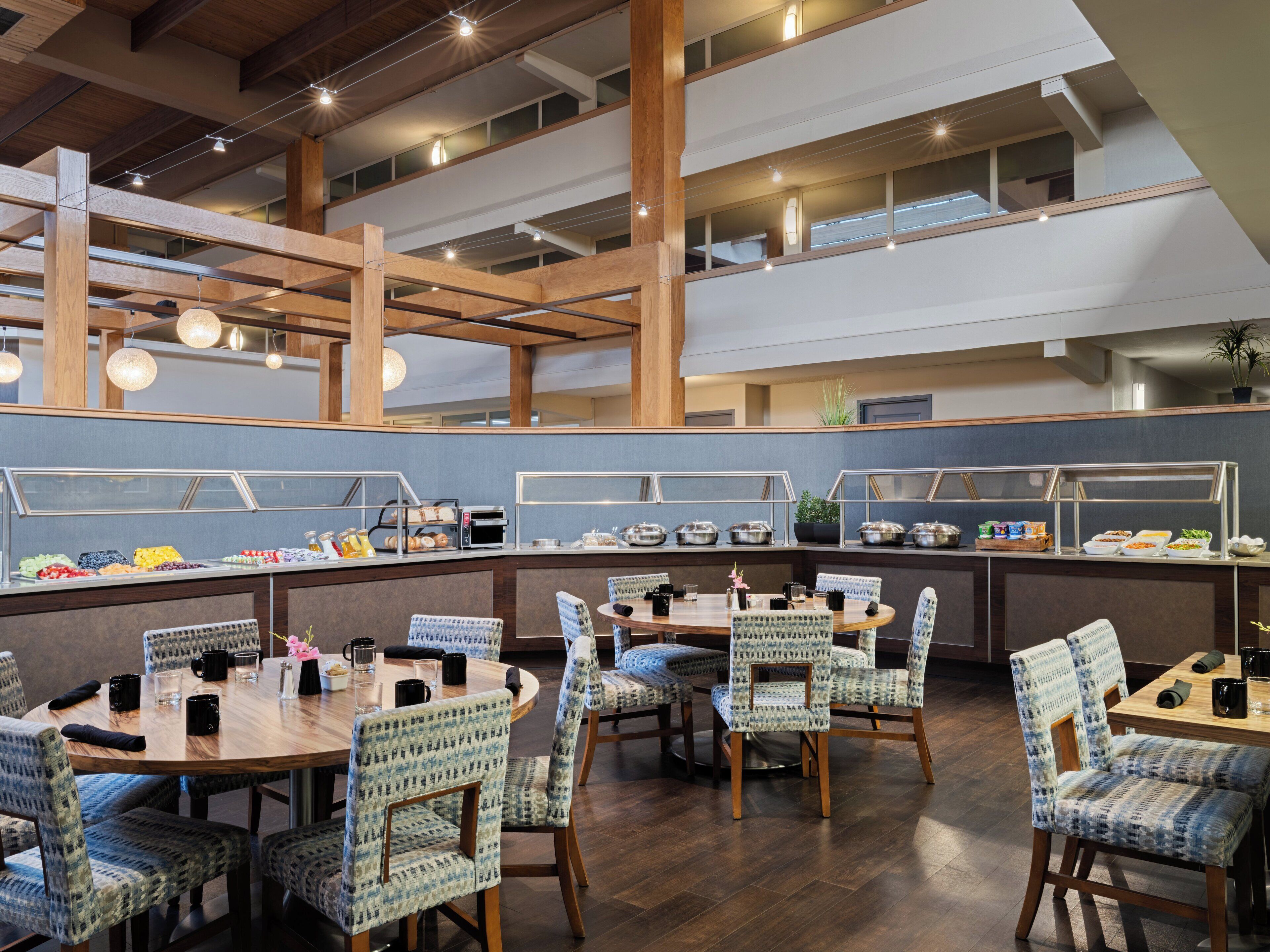 Un'area buffet con diverse opzioni gastronomiche, tavoli in legno e sedie a fantasia.