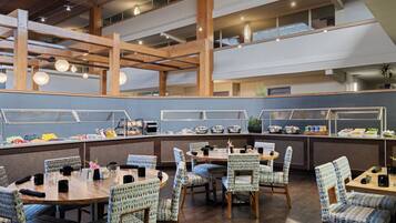 Un'area buffet con diverse opzioni gastronomiche, tavoli in legno e sedie a fantasia.