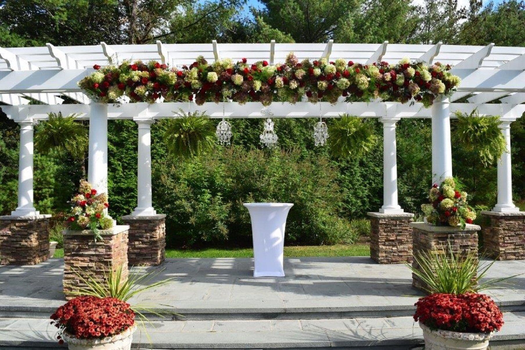 Una pérgola blanca con arreglos florales y un pedestal blanco en el centro.