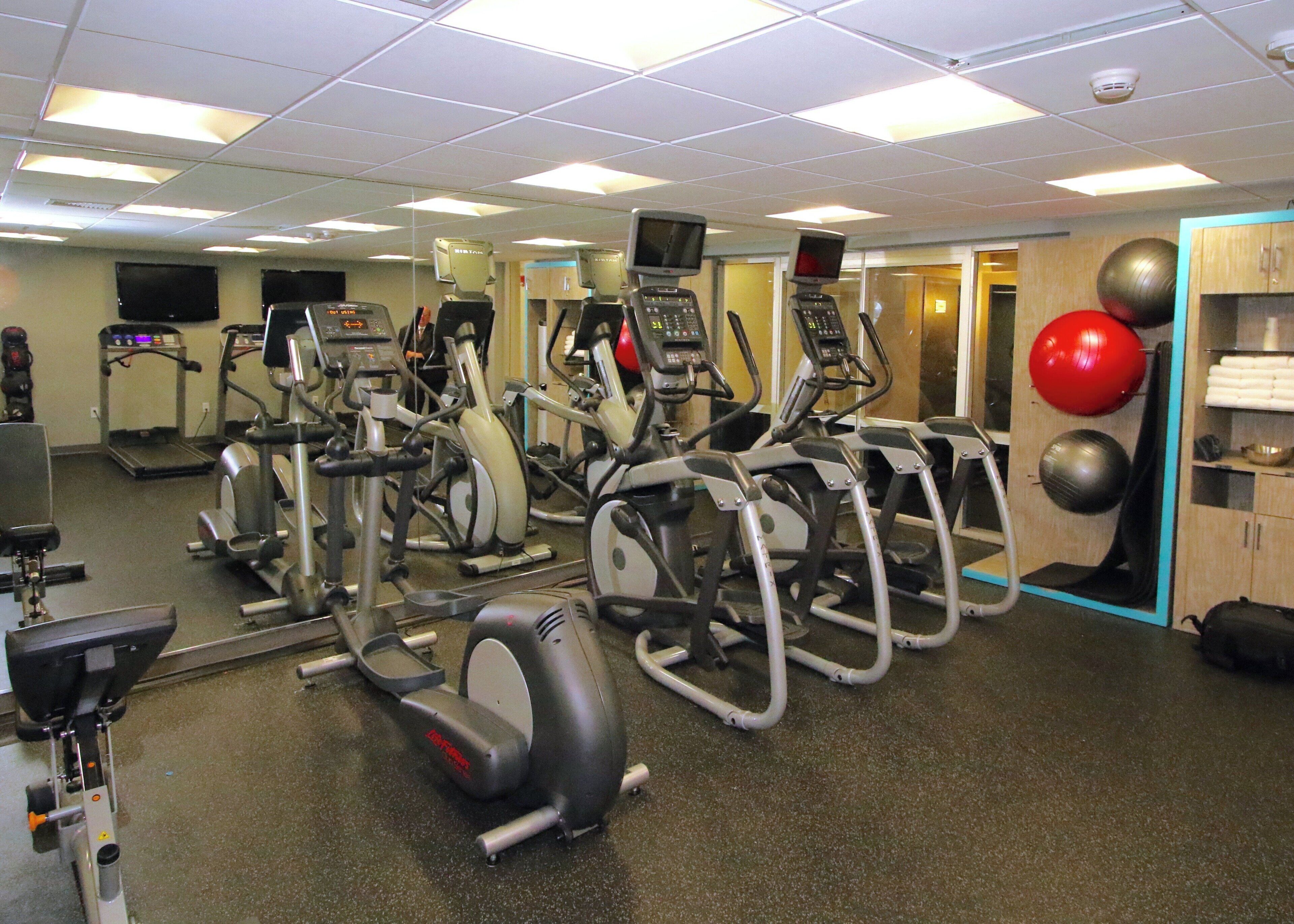 A gym with various exercise machines, a treadmill, and a mirrored wall.