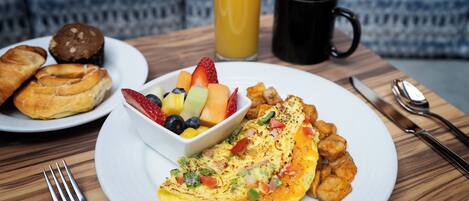 A breakfast setting with a plate of eggs, toast, and fruit, a glass of orange juice, and a black mug on a wooden table.