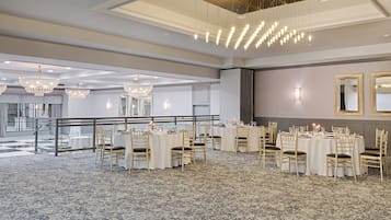 A spacious banquet hall with multiple round tables, elegant chandeliers, and a patterned carpet.