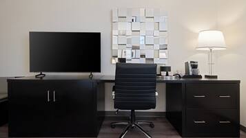 Un espacio de oficina moderno con una televisión de pantalla plana, una silla de oficina negra, un escritorio con cafetera y una pared decorativa con espejos.