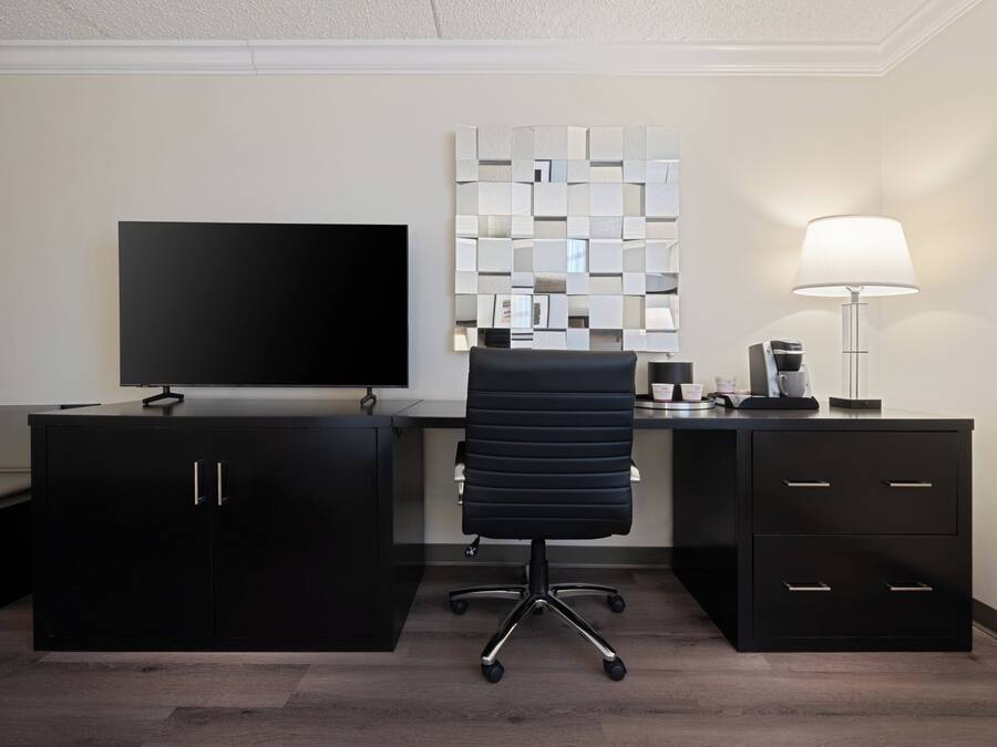 A modern office space with a flat-screen TV, a black office chair, a desk with a coffee maker, and a decorative mirror wall.