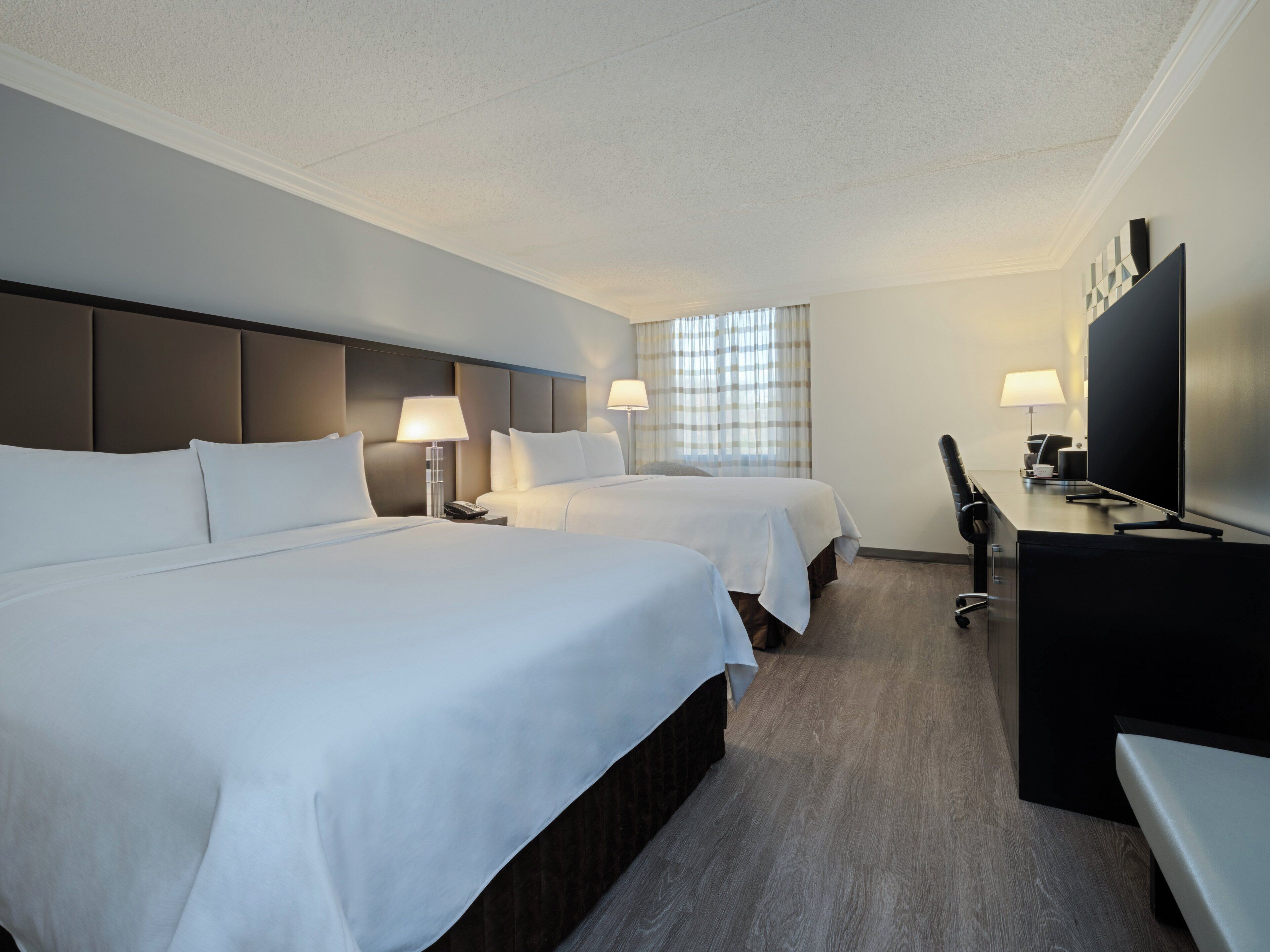 A hotel room with two beds, a desk, a TV, and a window with curtains.