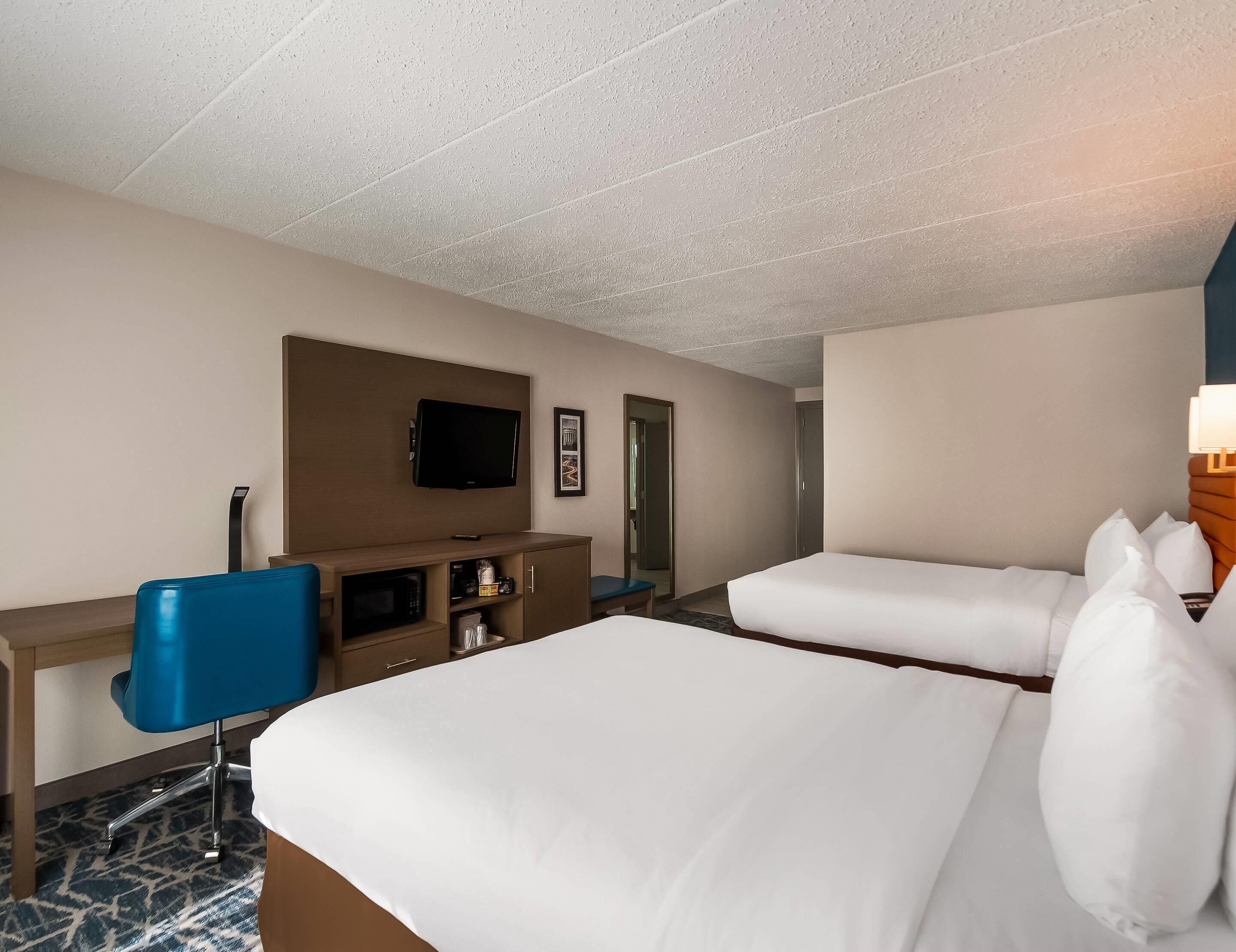 A hotel room with two beds, a desk with a chair, a television, and a microwave.