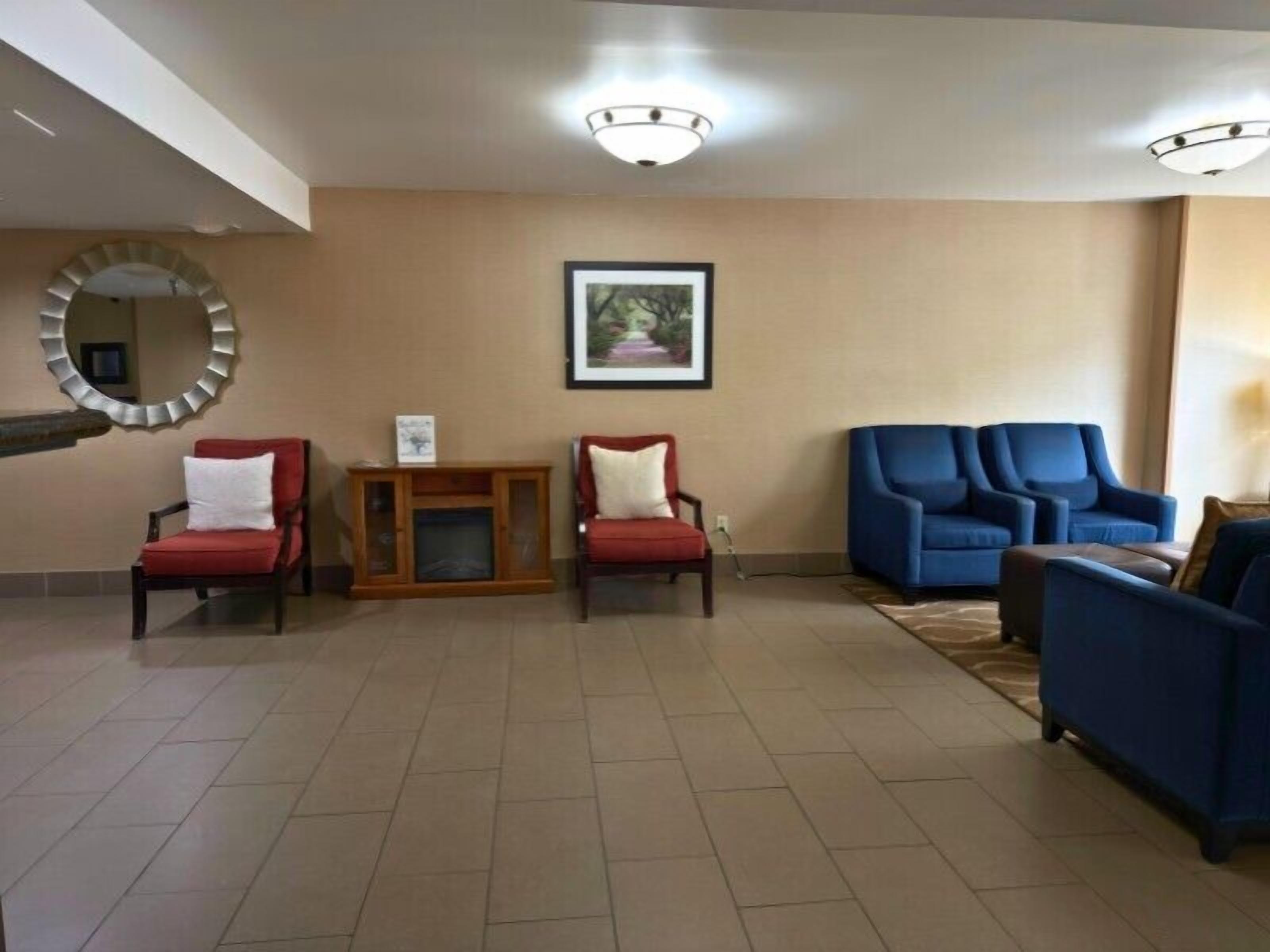 A spacious lobby with a wooden console table, two red armchairs, and a blue sofa set.