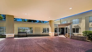 Un vaste espace extérieur doté d’une terrasse en briques, d’un coin salon abrité et d’un bâtiment avec de grandes fenêtres et un toit plat.