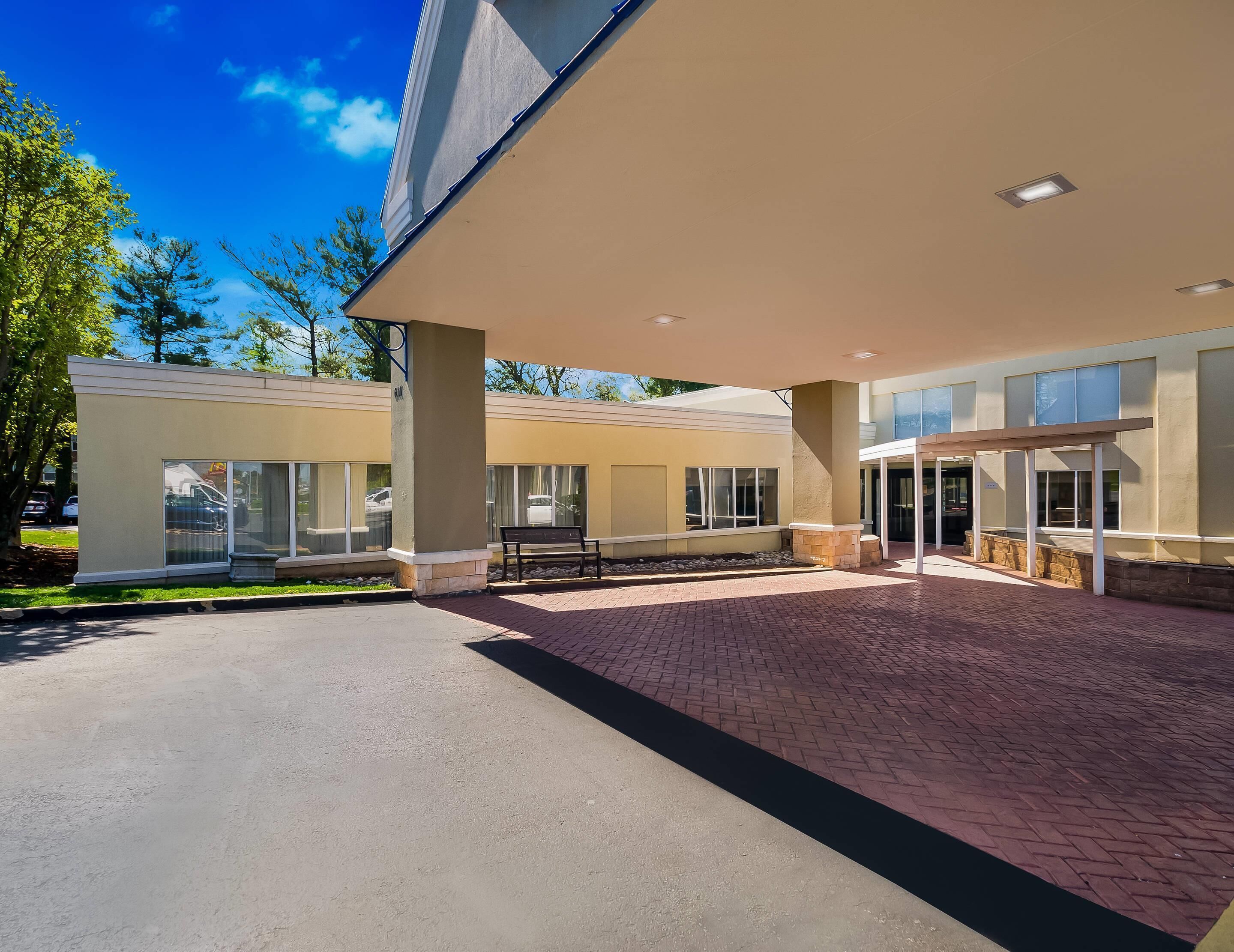 A modern building with a covered entrance, large windows, and a paved driveway.