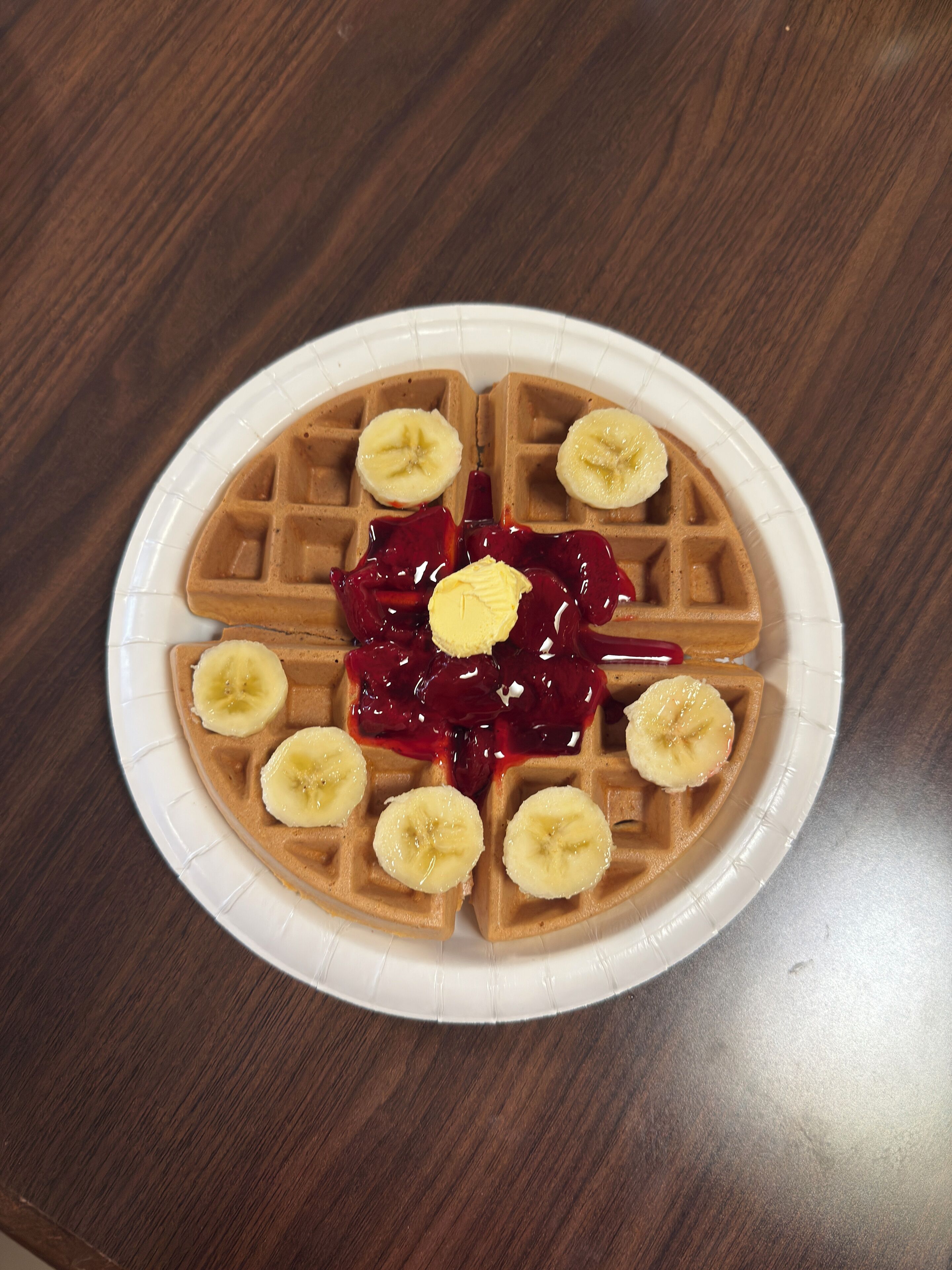 A plate with a waffle, banana slices, and red jam.