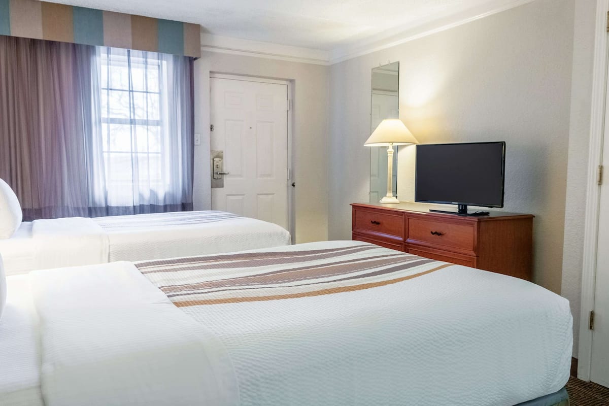 A hotel room with two beds, a television on a wooden dresser, a mirror, and a door.