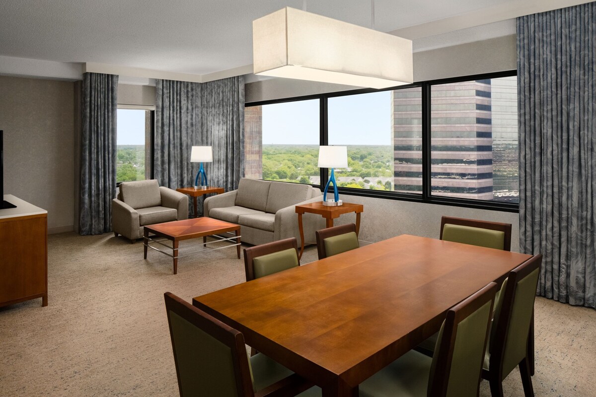 A hotel room with a large wooden dining table, two sofas, a coffee table, and a TV.