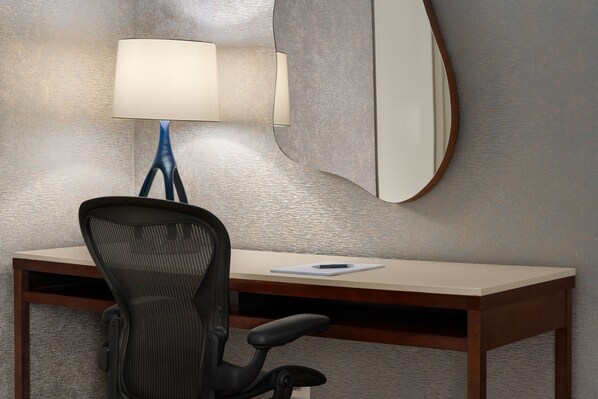 A desk with a chair, a lamp, and a mirror on the wall.