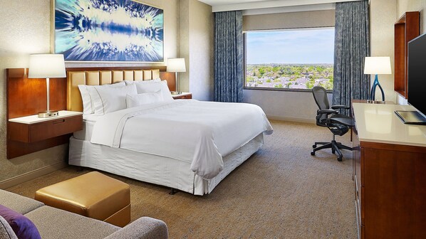 A hotel room with a large bed, a desk, a chair, and a view of the city.