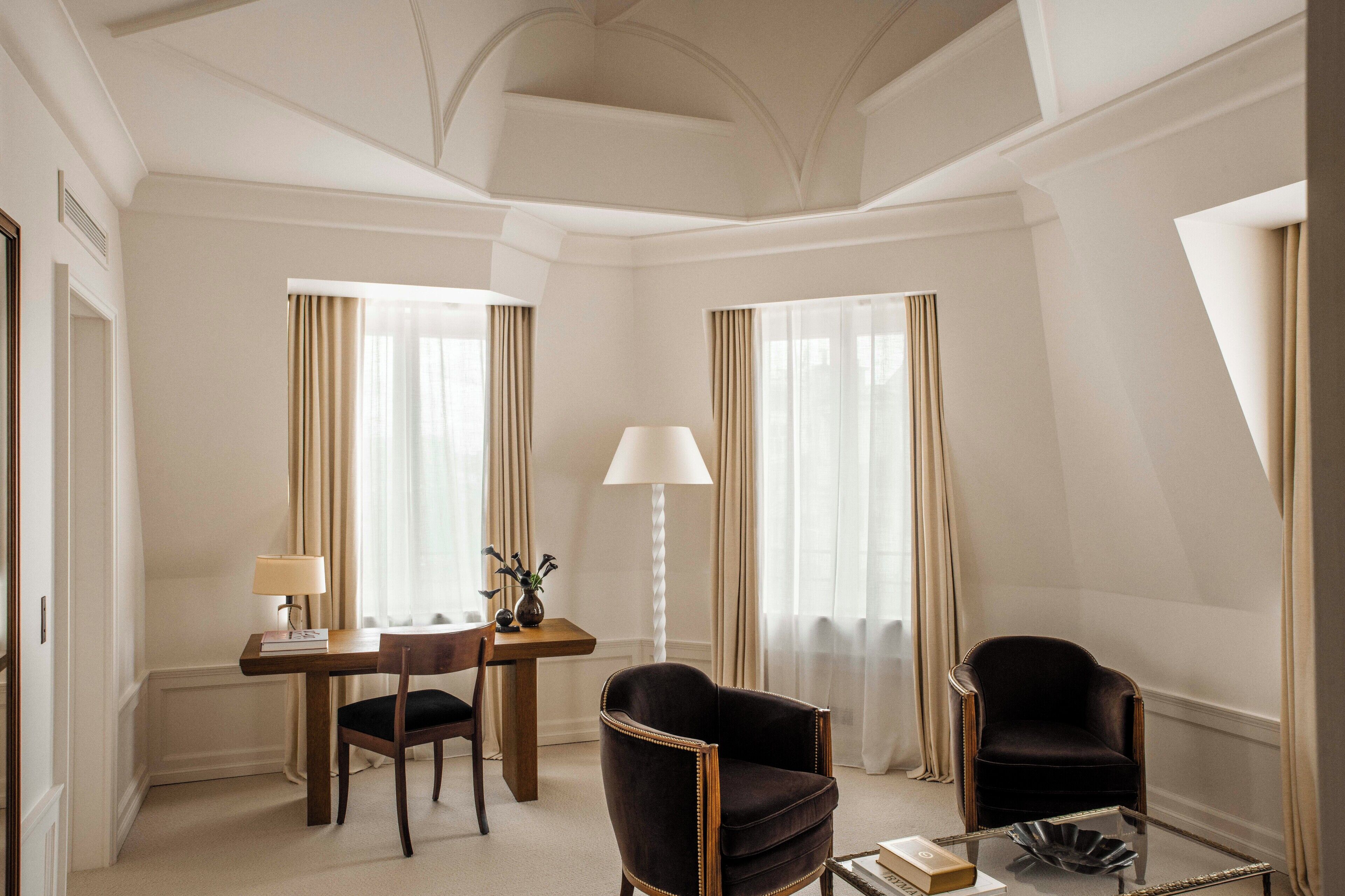 A hotel room with a wooden desk, two chairs, a lamp, and a glass coffee table.