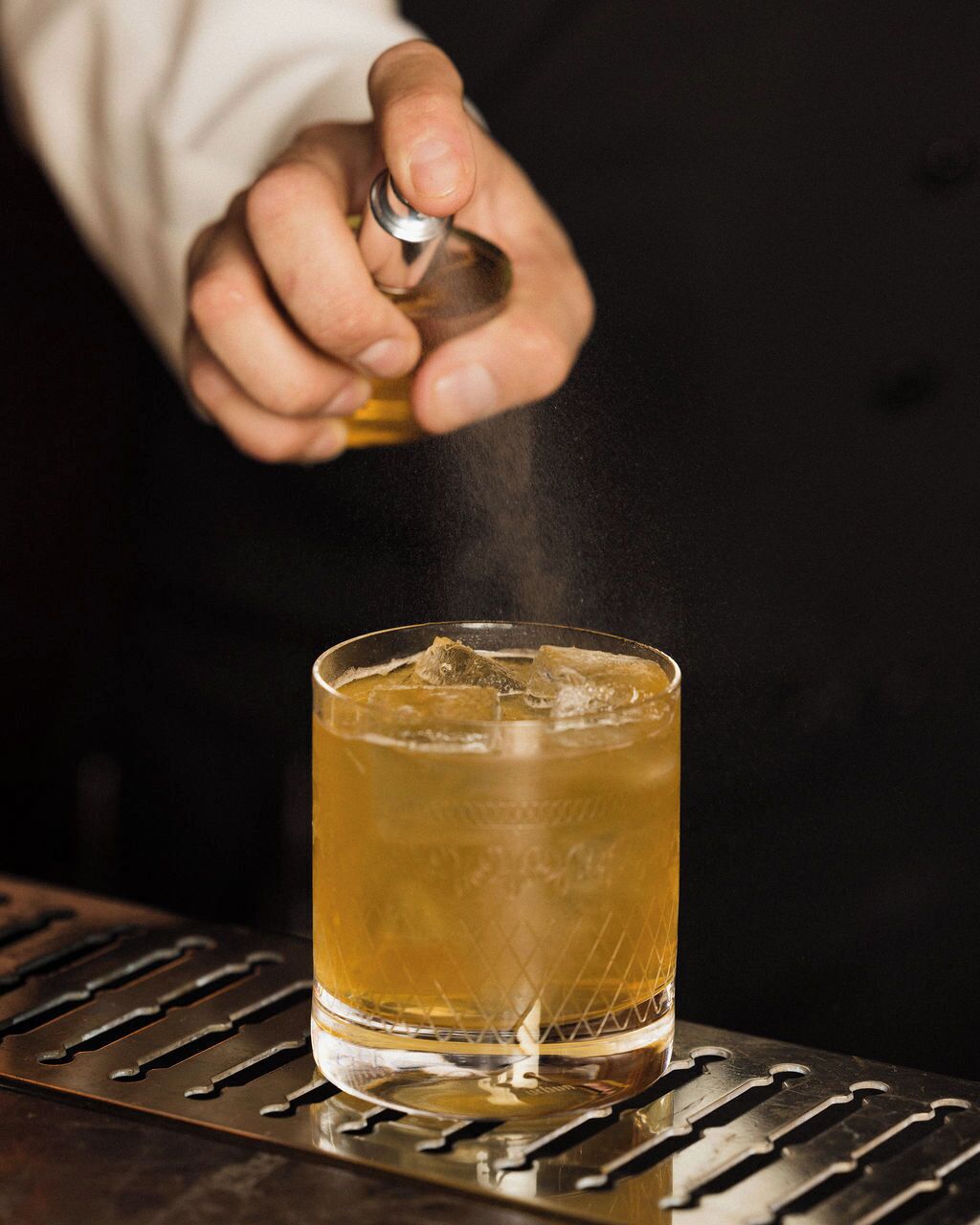 A person pouring a drink into a glass with ice cubes.