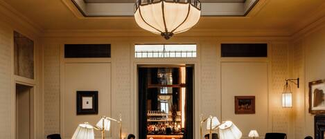 A spacious lobby with a high ceiling, a central seating area with sofas and armchairs, a chandelier, and a patterned carpet.