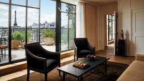 Amplia habitación con grandes ventanales que ofrecen vista a la Torre Eiffel, dos sillones de cuero negro, una mesita de centro de madera y una pequeña escultura sobre un pedestal.