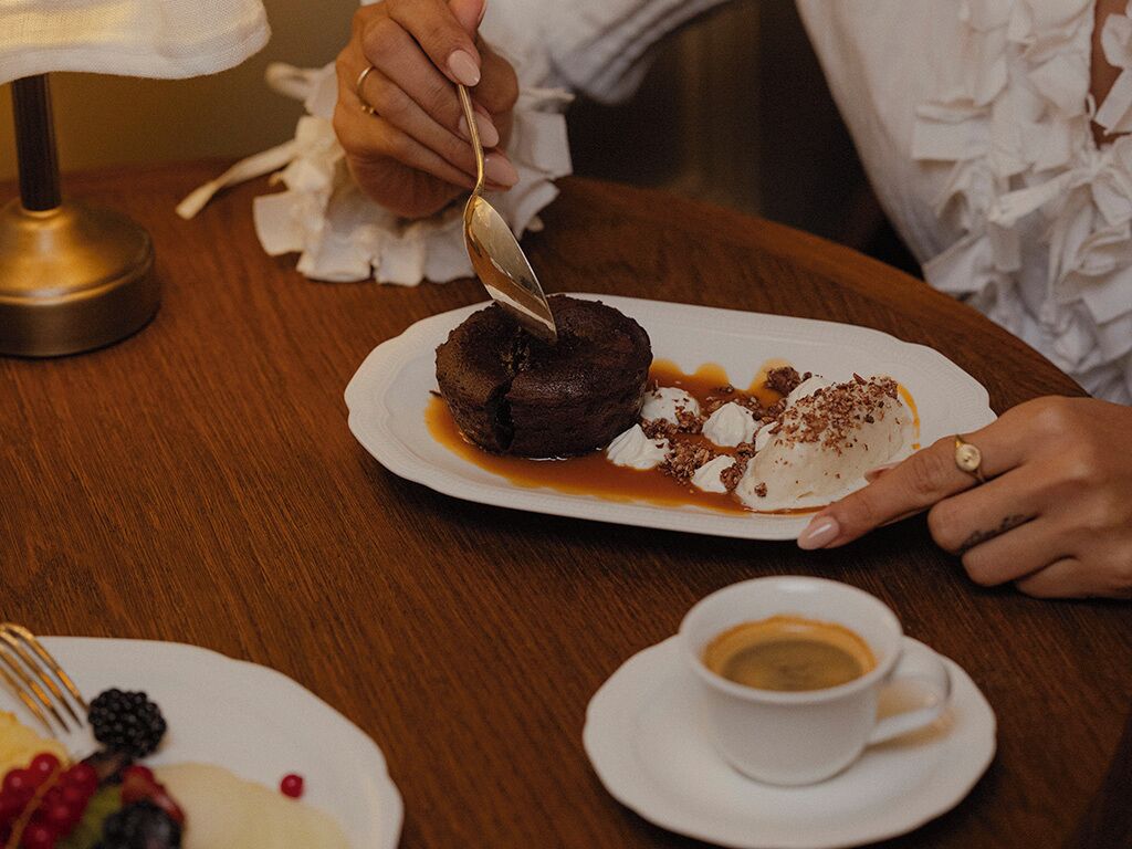 A dessert plate with a chocolate cake, whipped cream, and caramel sauce, a cup of coffee, and a fork on a wooden table.