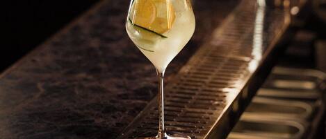 A bartender pouring a drink into a martini glass on a bar.