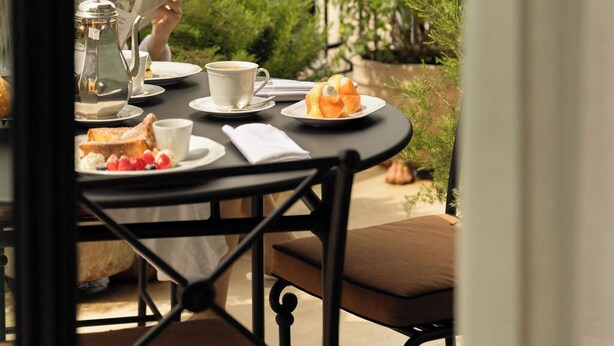 Un balcón con una mesa dispuesta para el desayuno, que incluye una cafetera, tazas y bollería.