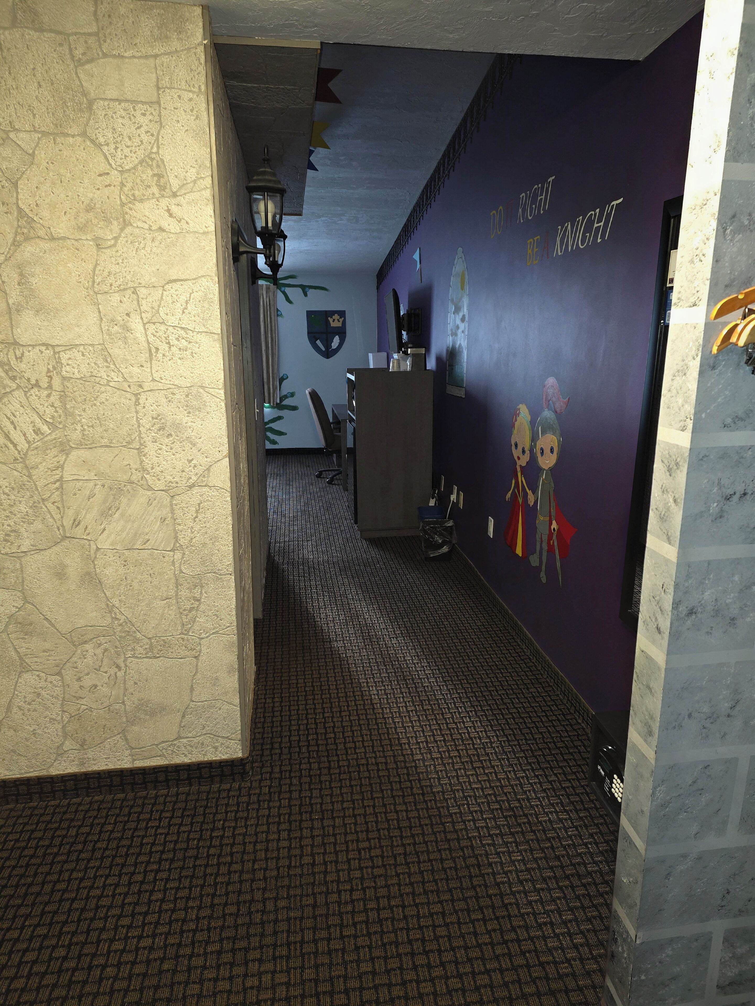 A hallway with a stone wall, a purple wall with a knight mural, and a patterned carpet.