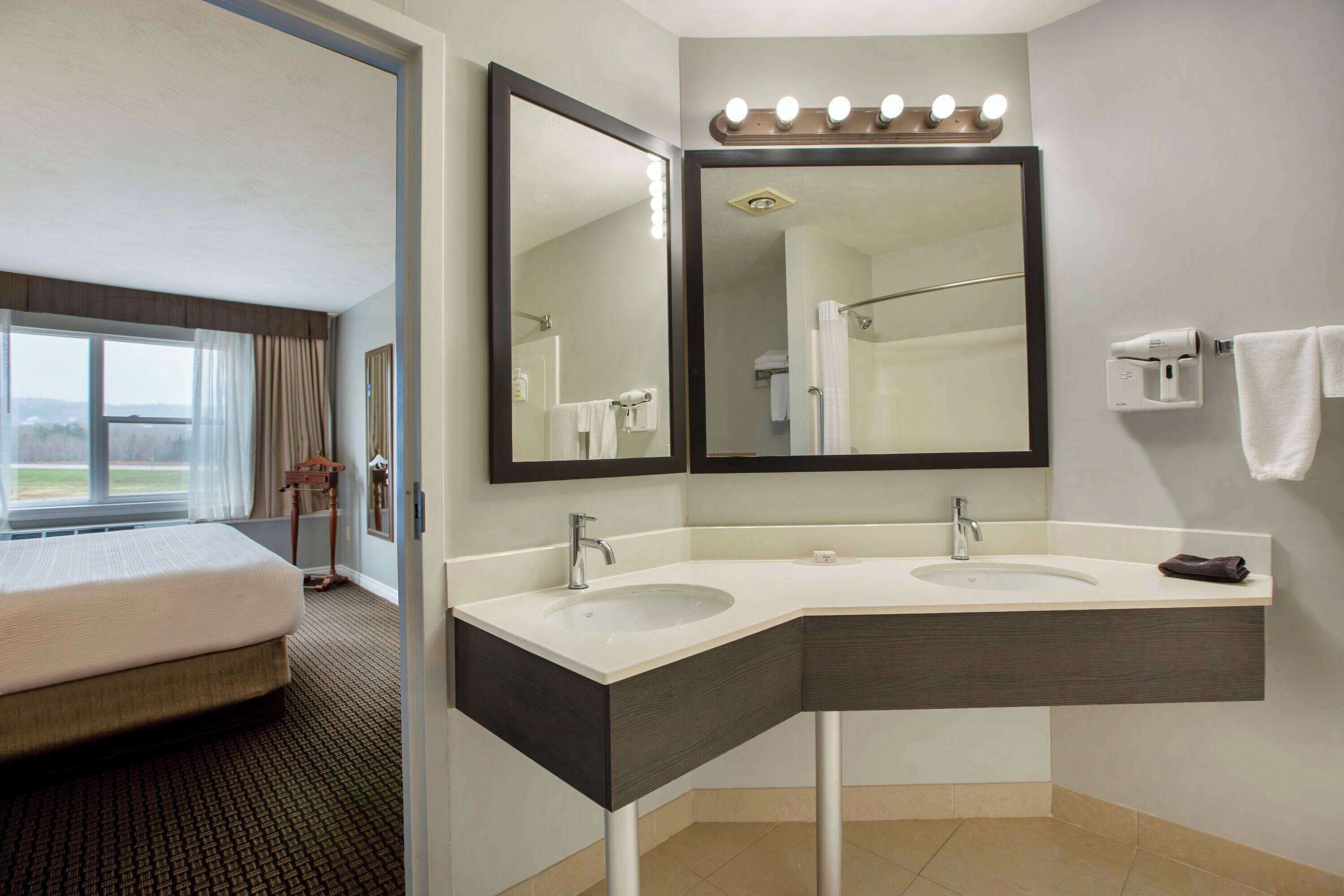 A hotel bathroom with two sinks, a large mirror, and a shower.