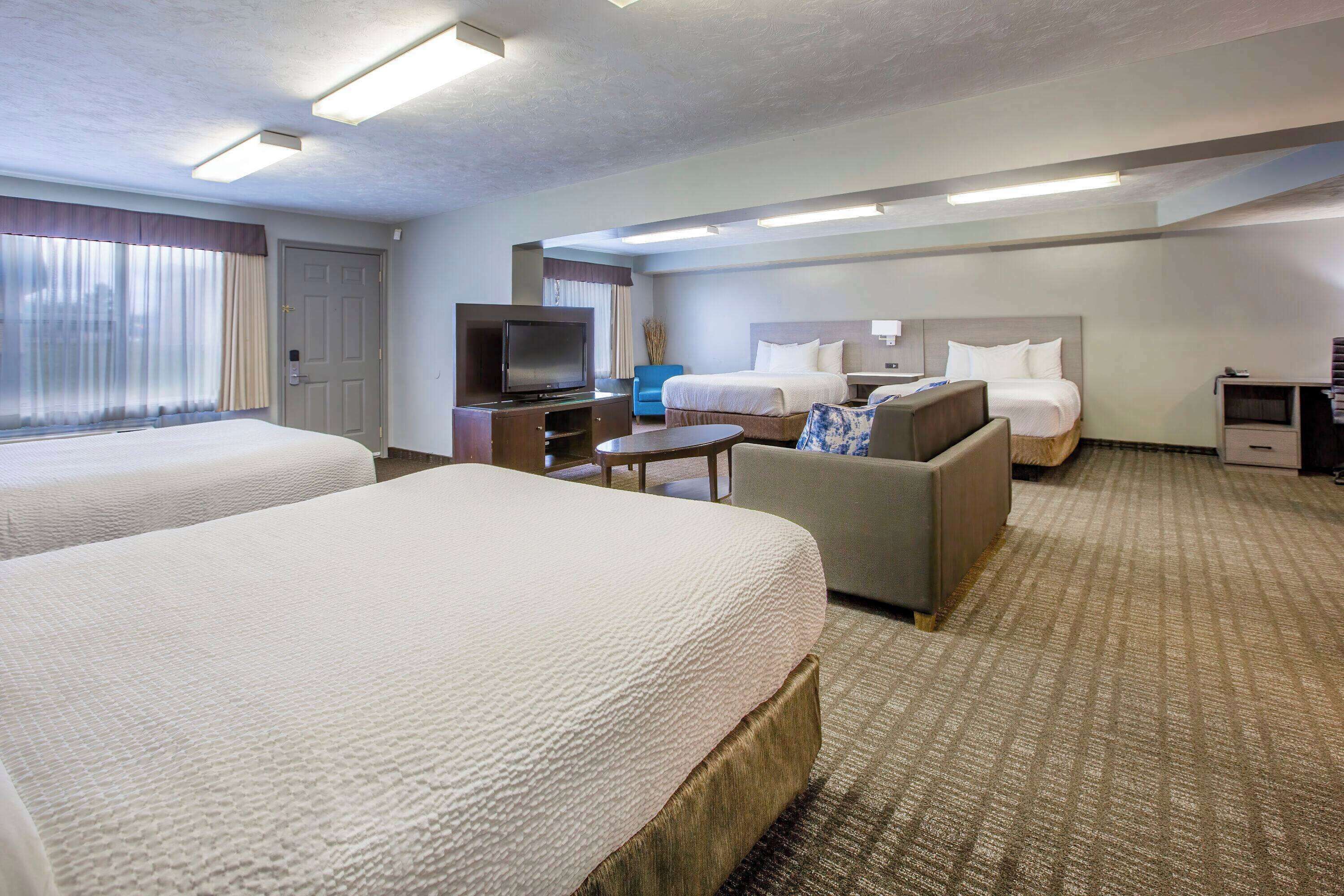 A hotel room with two beds, a TV, a sofa, and a small table.