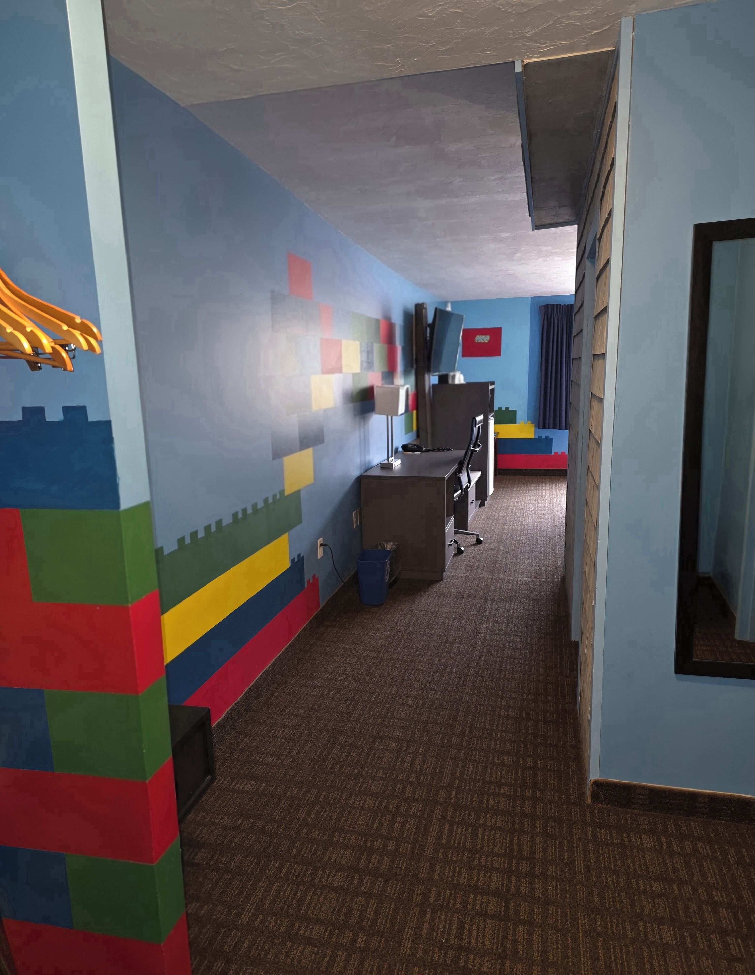 Un pasillo con una pared de LEGO, un escritorio con computadora y una ventana con cortina.