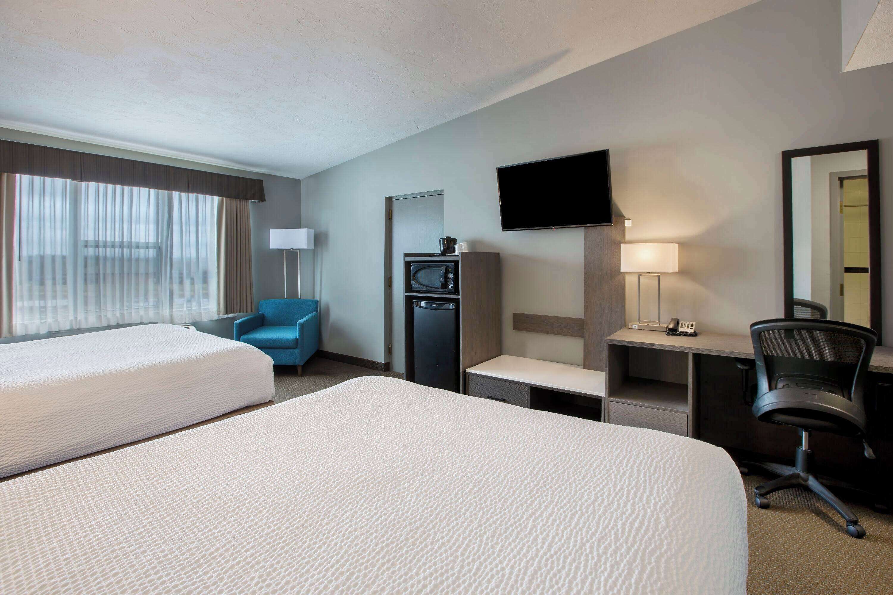 A hotel room with two beds, a desk, a chair, a television, a microwave, and a lamp.