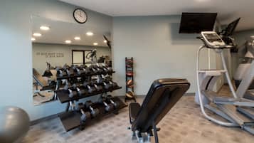 Uma academia com equipamentos de exercício, um espelho, um relógio e uma televisão na parede.