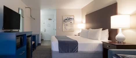 A hotel room with a bed, bedside table, lamp, TV, and a desk with drawers.