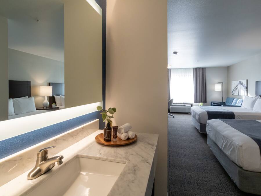 Habitación de hotel con lavamanos de mármol, un espejo grande y una cama con cabecera oscura.