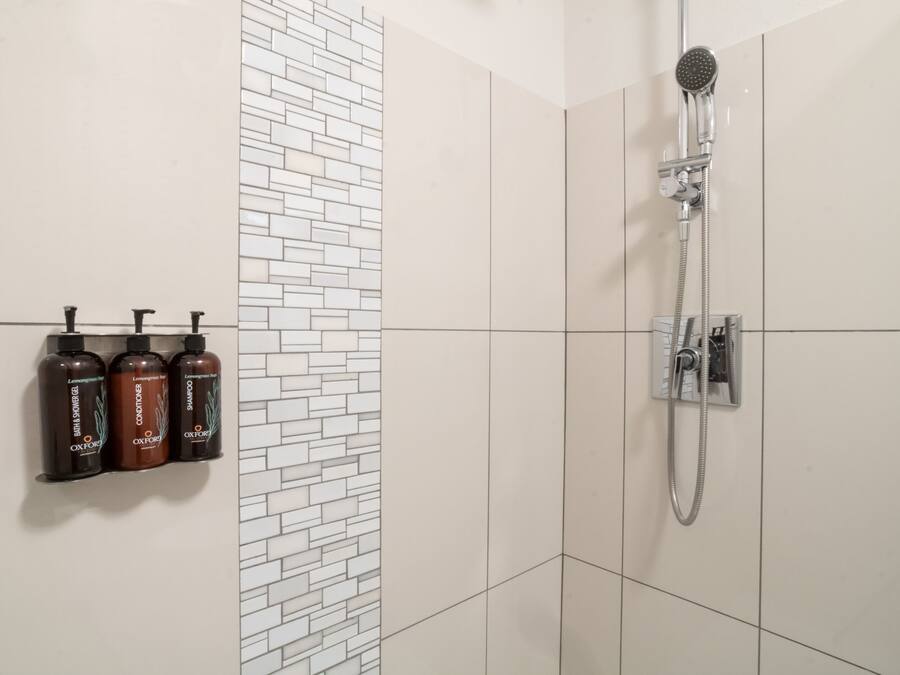 Une salle de bain avec une douche, trois bouteilles de shampoing et un mur carrelé.