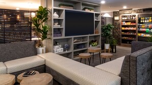 A modern living room with a sectional sofa, a flat-screen TV, a bookshelf, and a small bar area. - Oxford Suites Portland - Jantzen Beach (Portland)