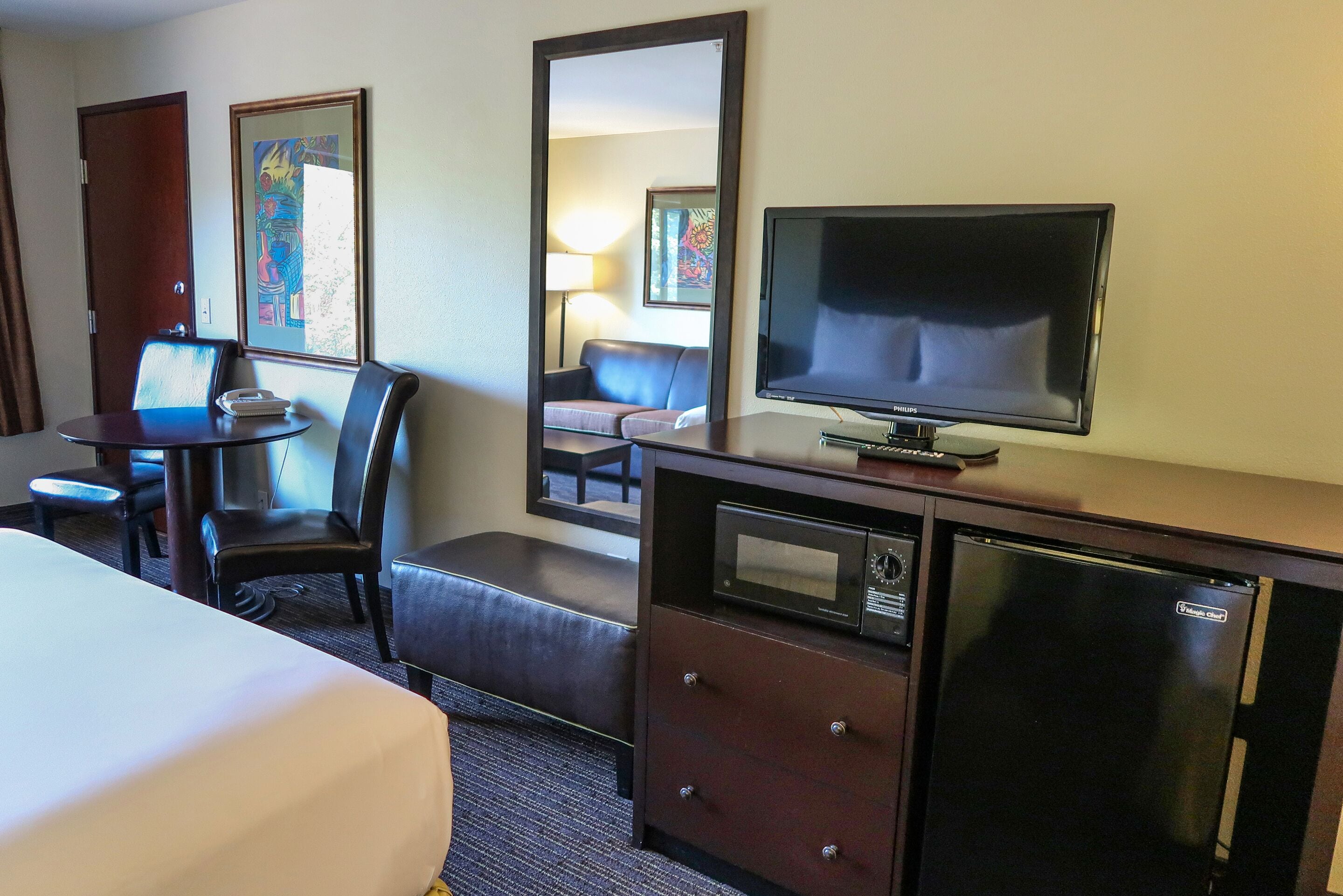 A hotel room with a bed, a desk with a telephone, a television, a microwave, and a refrigerator.