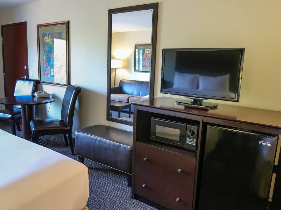 A hotel room with a bed, a desk with a telephone, a television, a microwave, and a refrigerator.