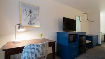 Habitación de hotel con escritorio, silla, televisor, cómoda y un cuadro en la pared.